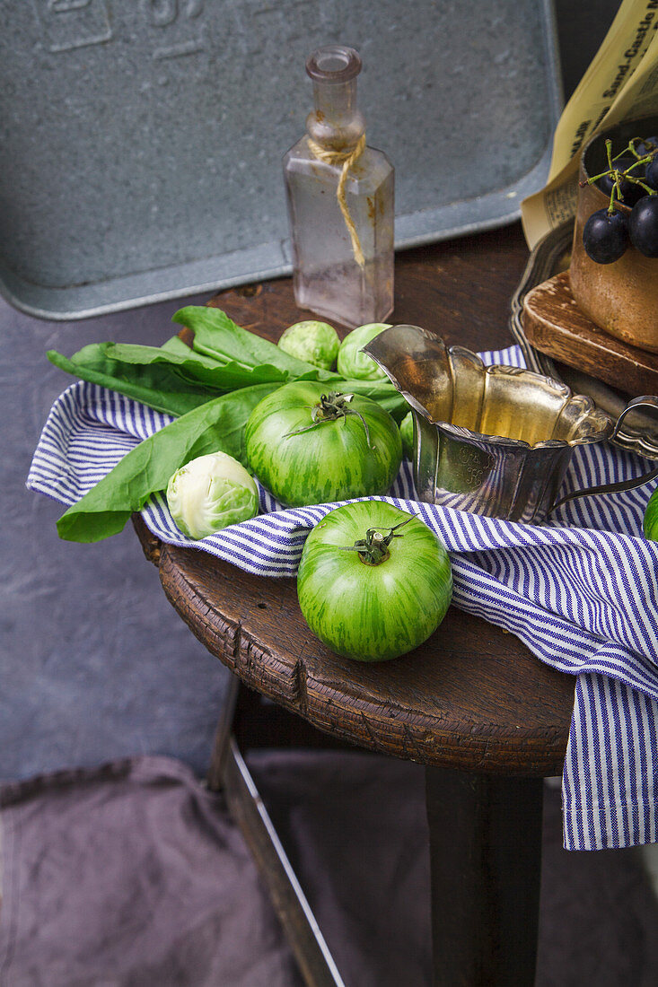 An arrangement of green tomatoes and Brussels sprouts on a wooden stool