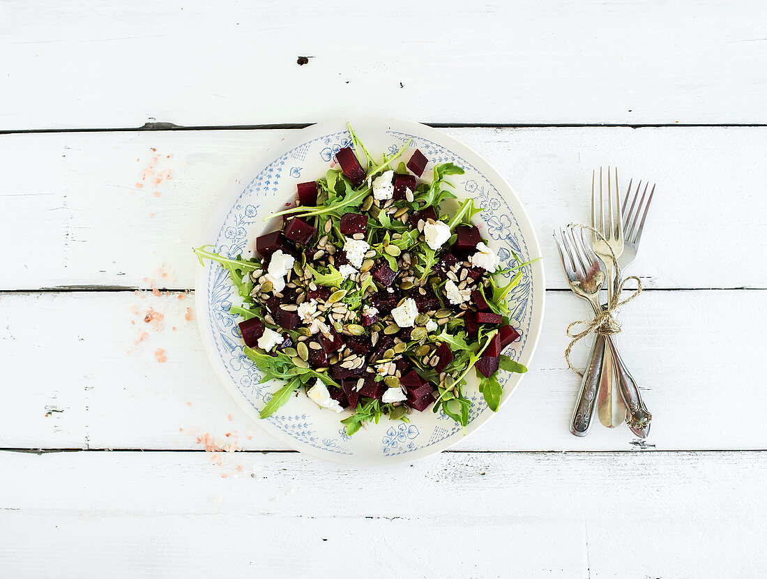 Beetroot salad with arugula, feta cheese and pumpkin seeds in vintage plate over white rustic wooden background