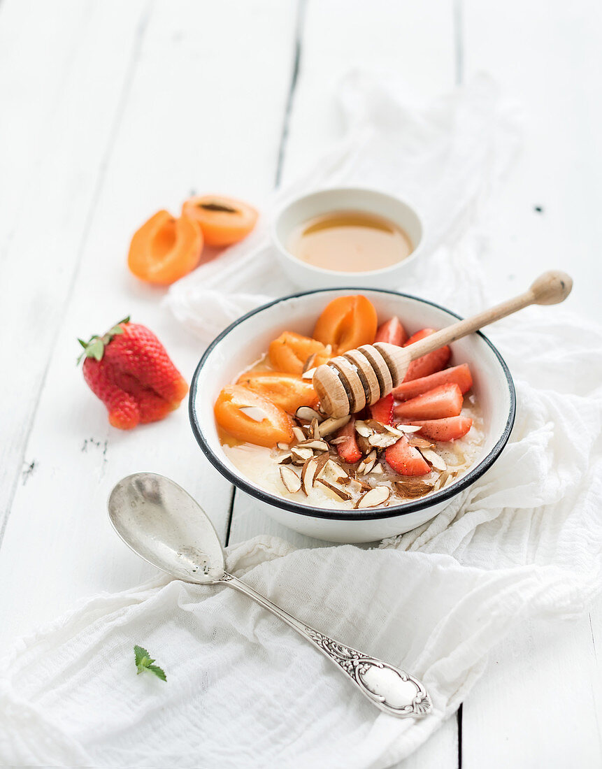 Healthy breakfast set. Rice cereal or porridge with fresh strawberry, apricots, almond and honey over white rustic wood backdrop
