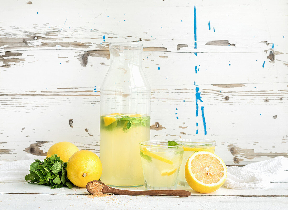 Fresh homemade lemonade with lemons and mint on white wooden backdrop