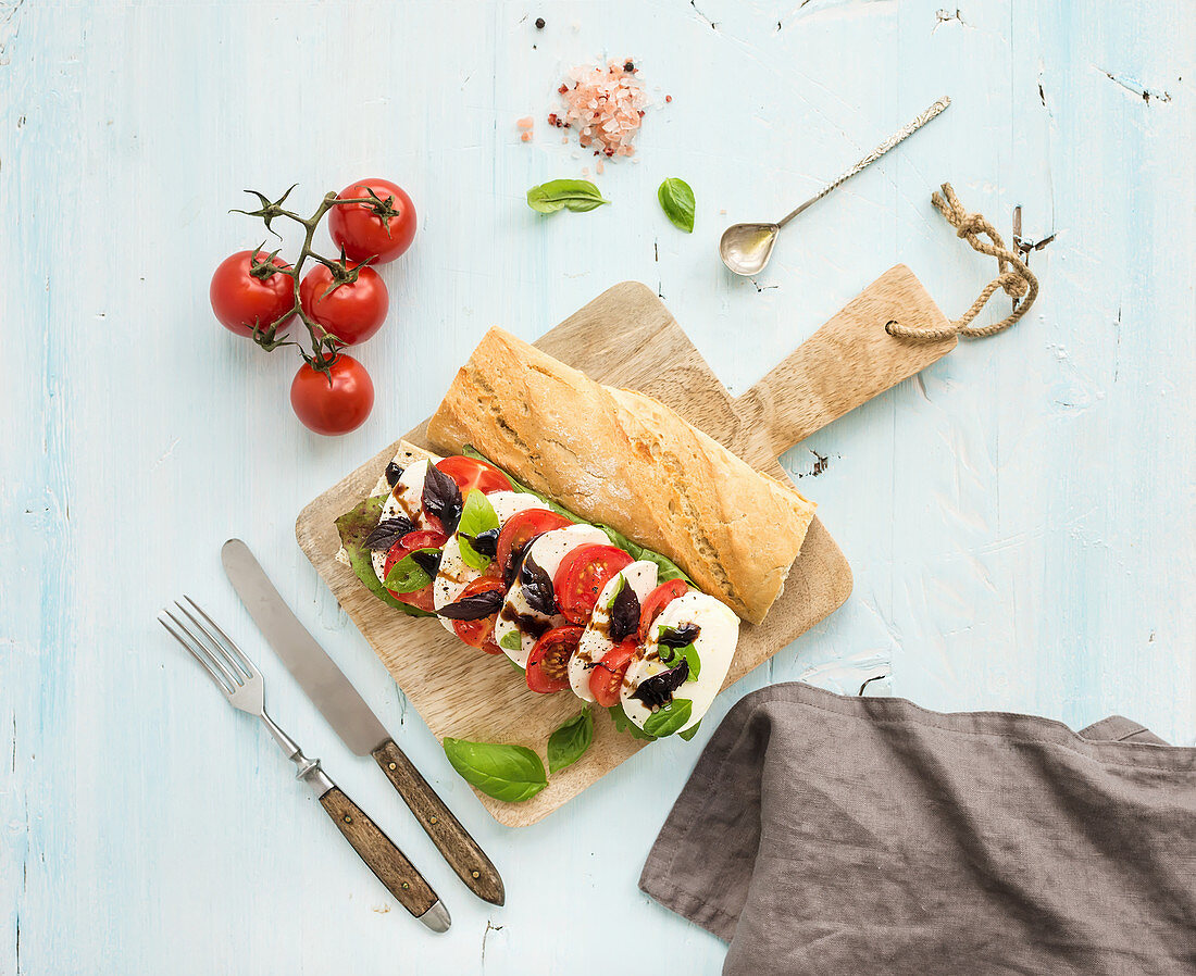 Tomato, mozzarella and basil sandwich on wooden chopping board over light blue background