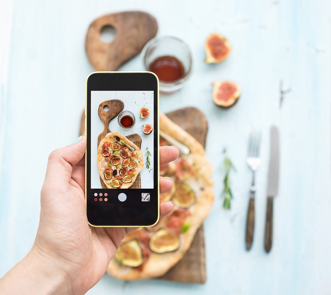 Hausgemachte Pizza wird mit Smartphone fotografiert