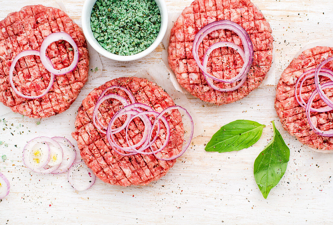 Raw ground beef meat cutlet for cooking burgers with onion rings and spices
