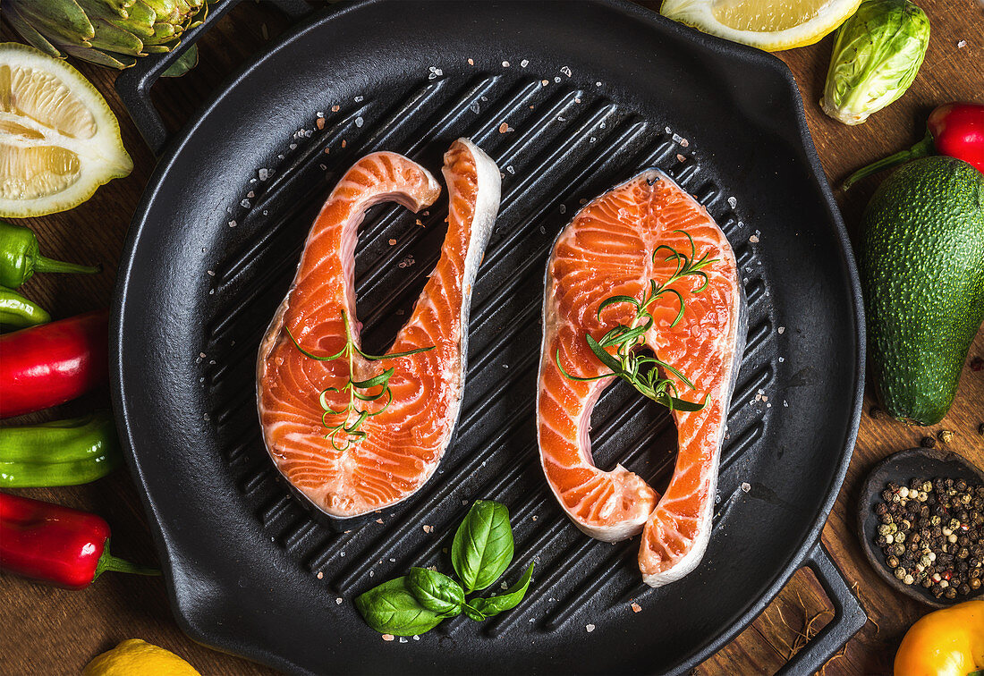 Uncooked salmon with vegetables, herbs, lemon, avocado, artichokes, spices in iron grilling pan