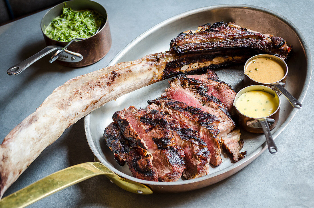 Geschnittenes Rindersteak mit Knochen, zwei Saucen und Spinat