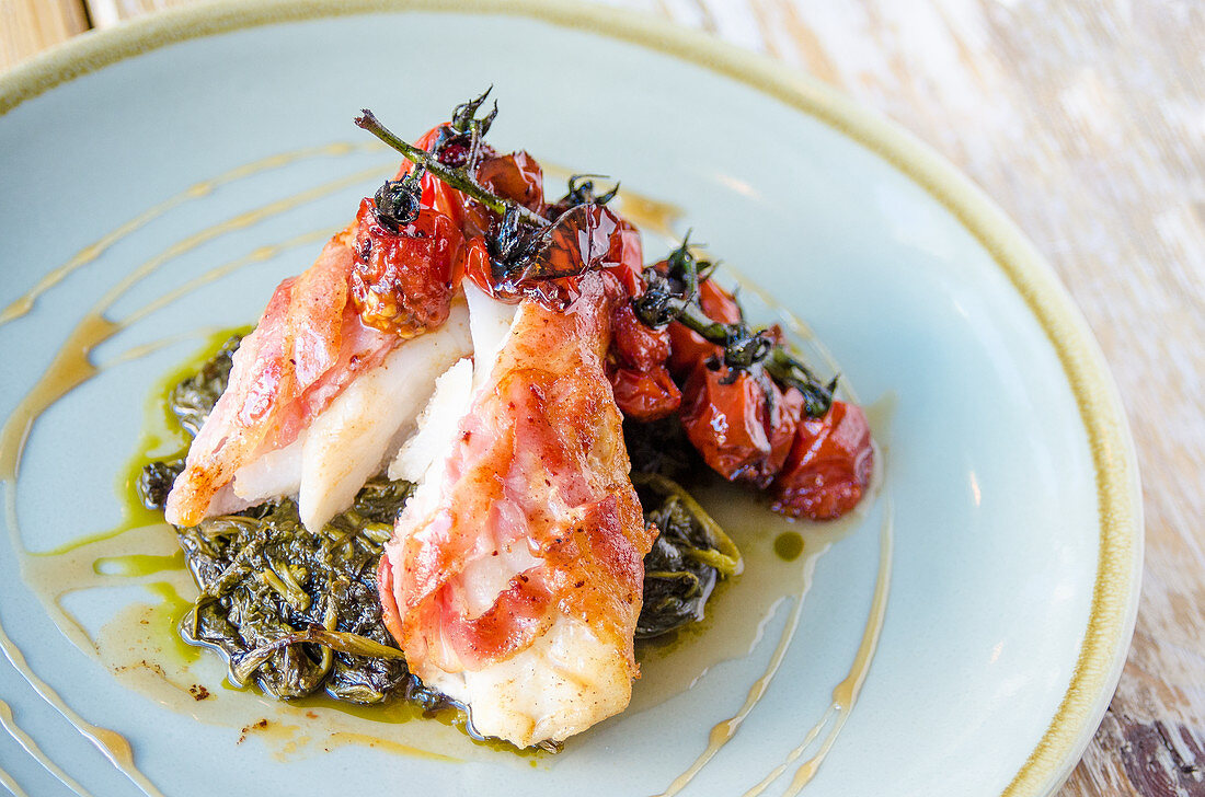 Cod fillet wrapped in bacon on a bed of spinach with grilled cherry tomatoes
