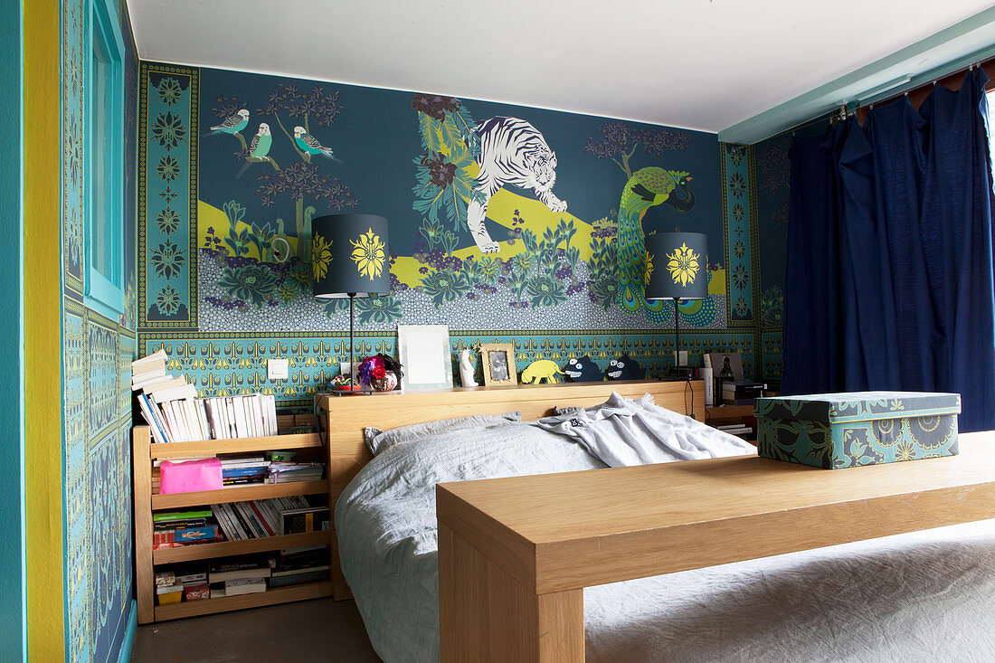 Bed with overbed table and shelf on headboard against ornate patterned wallpaper