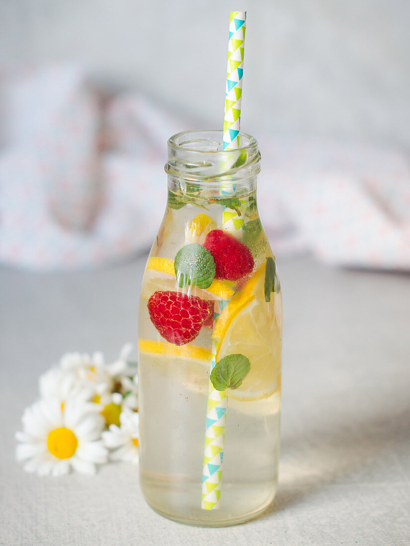 Holunderblütenlimonade serviert mit Früchten in Glasflasche