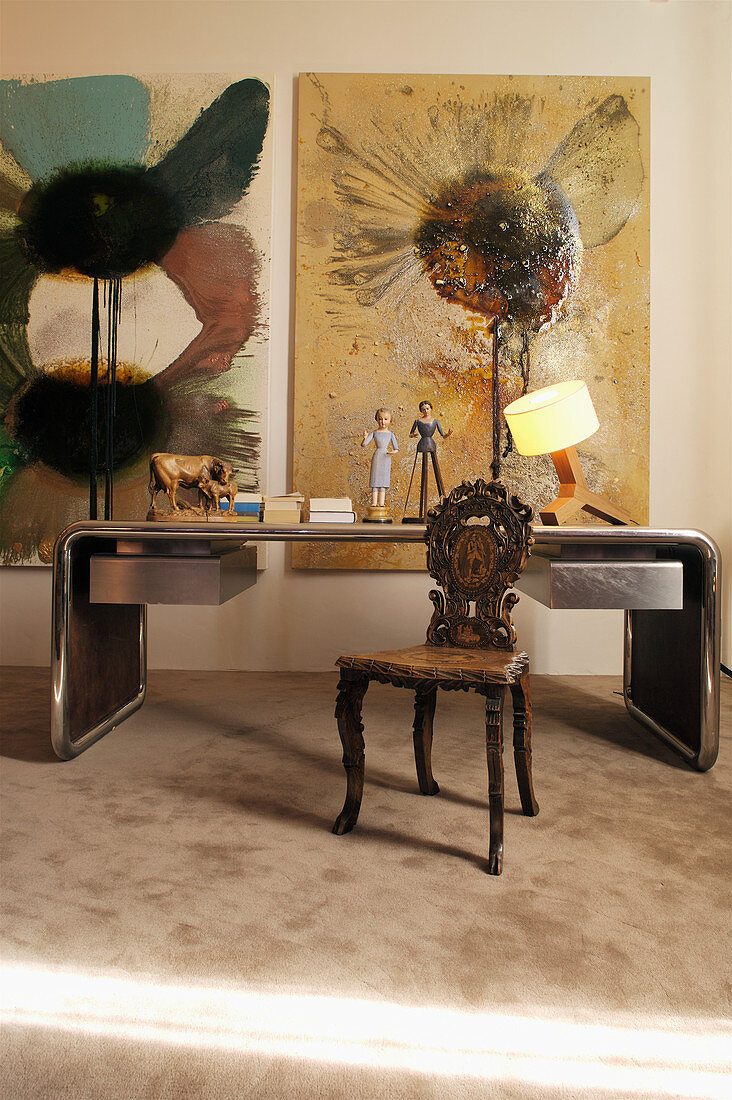 Desk with metal frame, antique carved wooden chair and modern artworks on wall