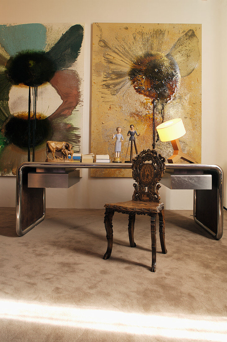 Schreibtisch mit Metallrahmen, antiker Holzstuhl mit Schnitzerei und moderne Kunst an der Wand