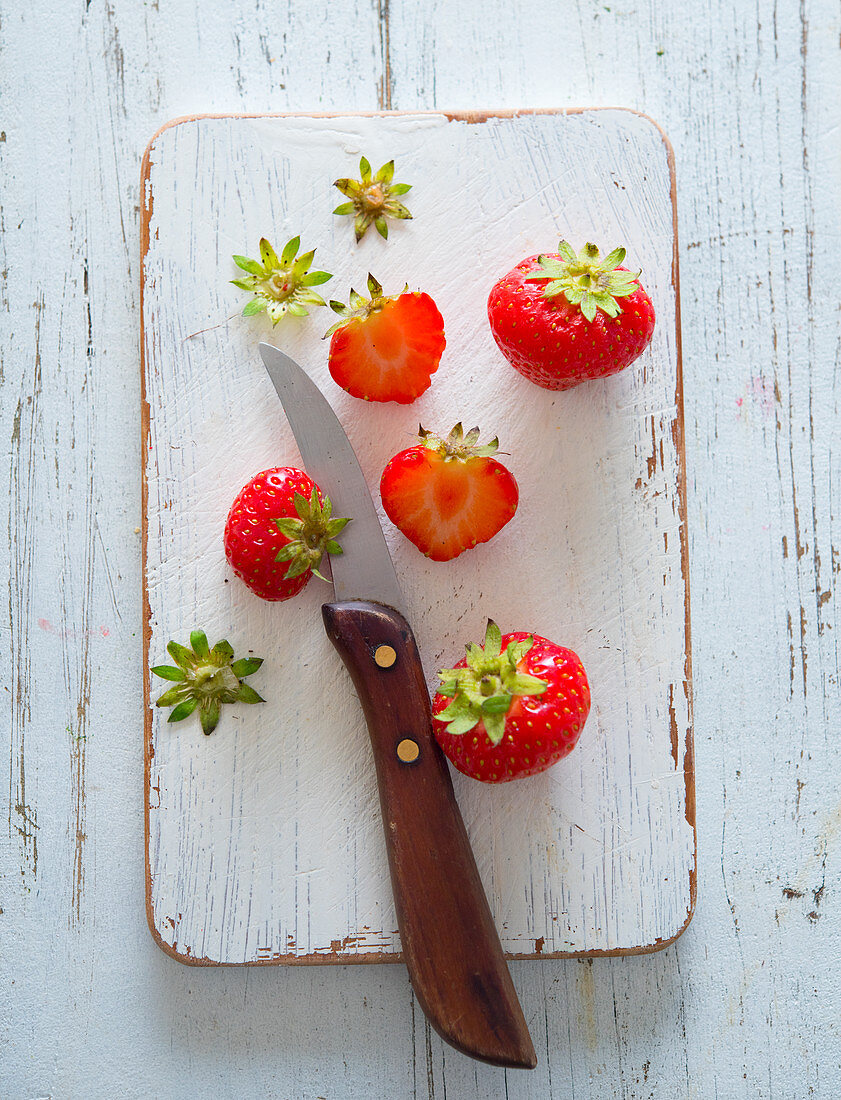Strawberries, partially prepared with a kitchen knife on a wooden board