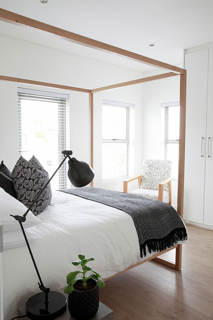 Four-poster bed in elegant bedroom with armchair and fitted wardrobe in background