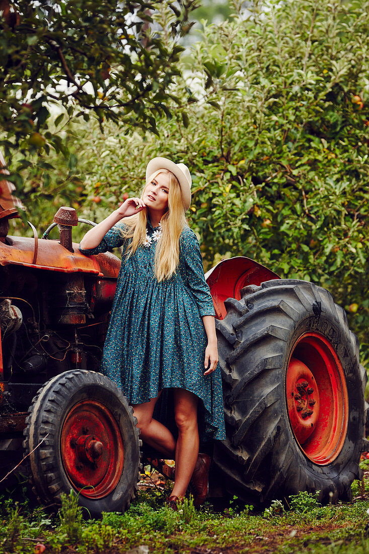 Blonde Frau in blauem Sommerkleid neben Traktor