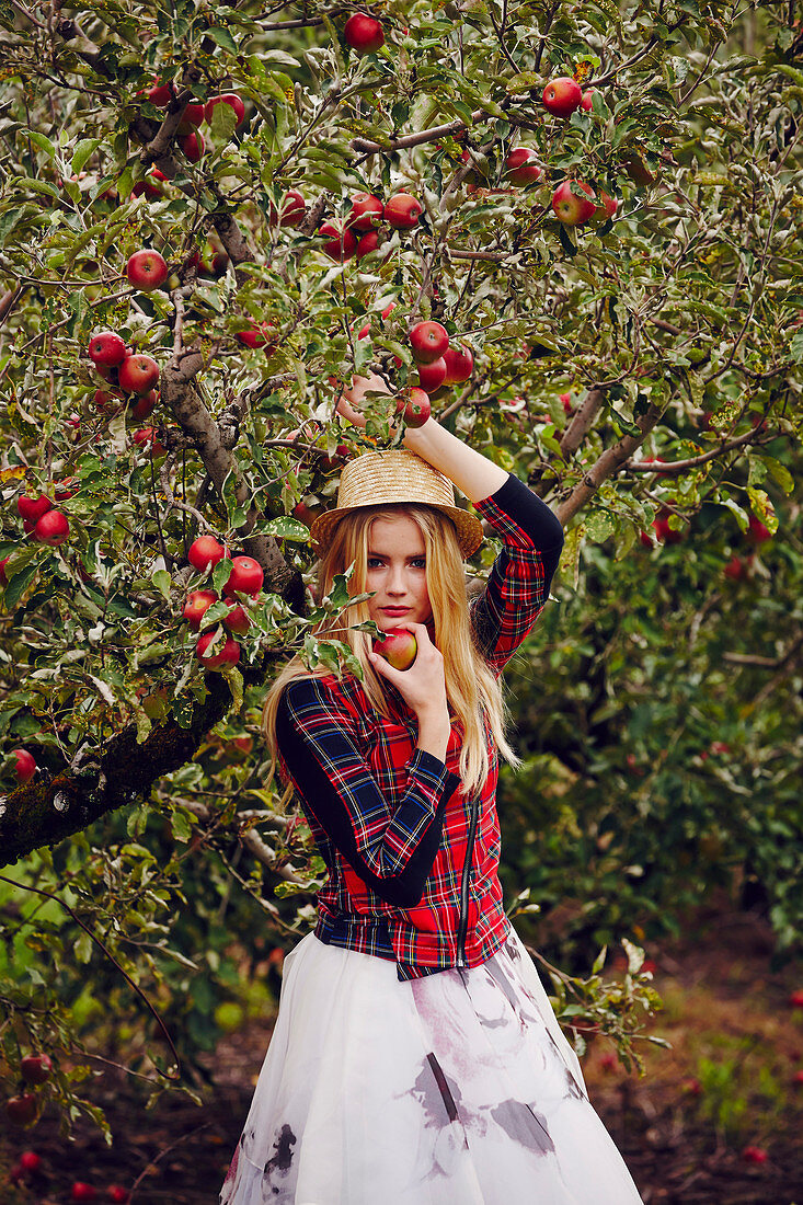 A blonde woman wearing a checked jacket and a tulle skirt by an apple tree