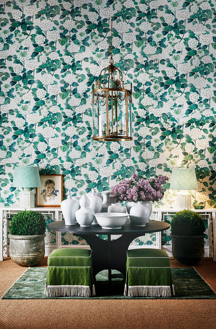 Green and white wallpaper with floral pattern, round table with white ceramics and lantern light