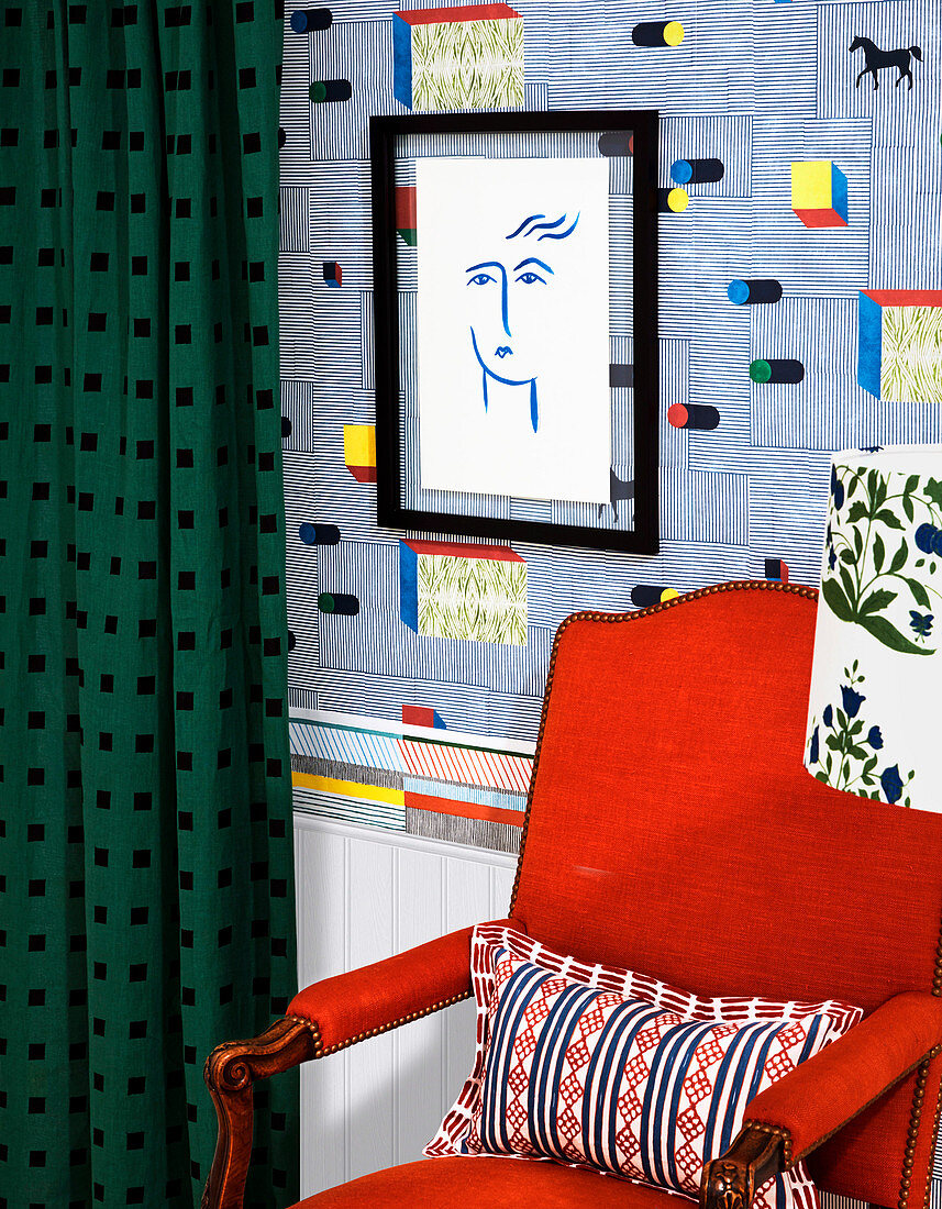 Red armchair in front of designer wallpaper and drawing in black frame