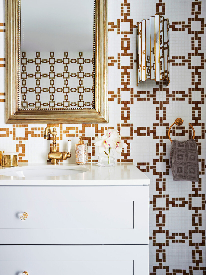 Gold frame mirror over white vanity in luxurious bathroom with gold and white mosaic tiles