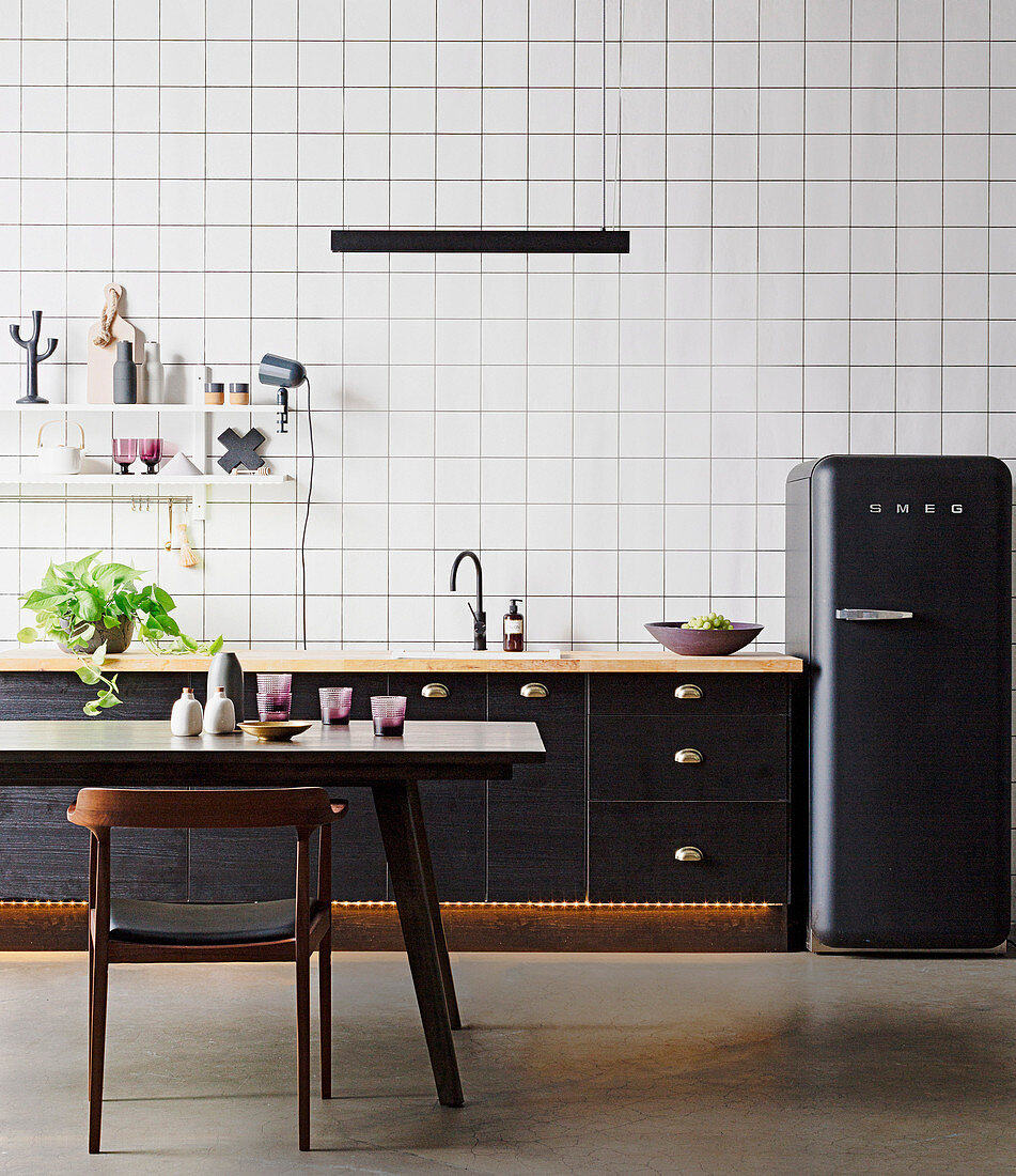 Black kitchen counter and black fridge in front of wallpaper with grid pattern, dining table and chair