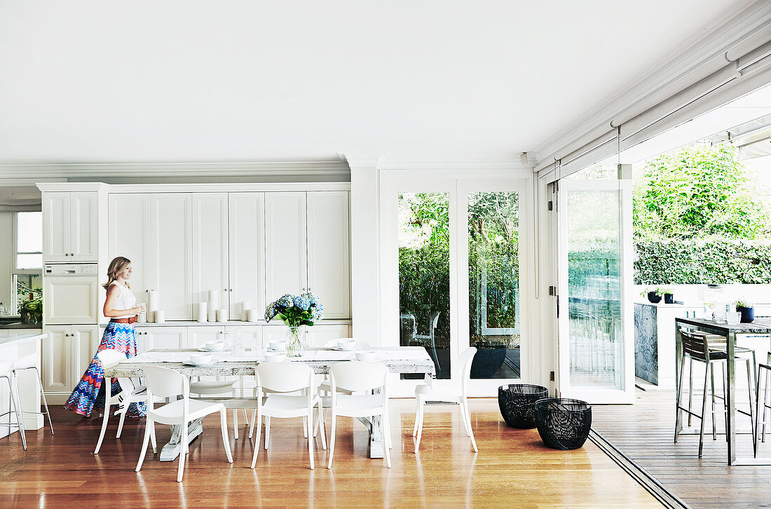Frau geht durch Wohnküche mit weißen Möbeln zur Terrasse