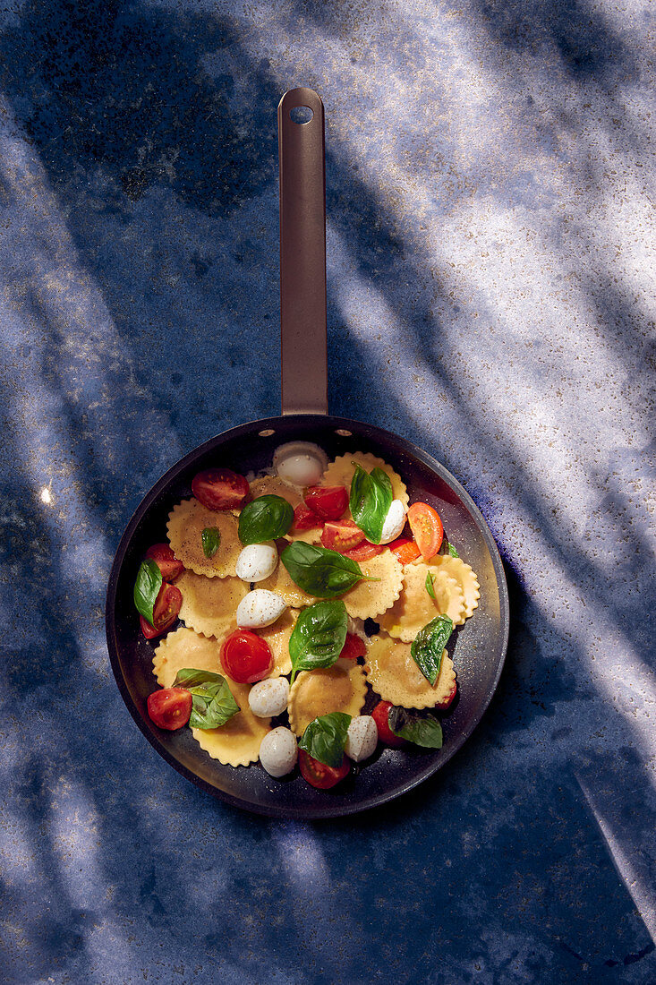 Ravioli mit Tomaten, Mozzarella und Basilikum in der Pfanne (Aufsicht)