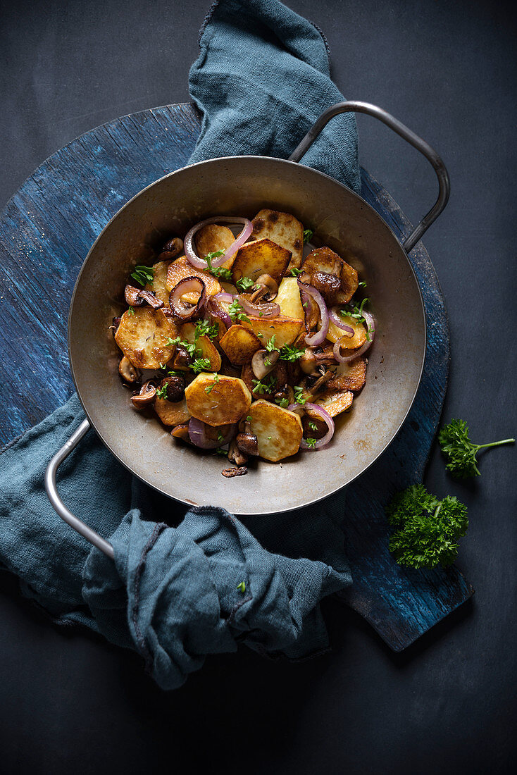 Fried potatoes with mushrooms and red onions in a serving pan