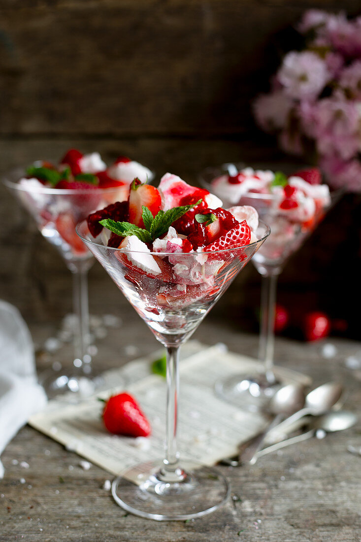 Fresh strawberries with pieces of strawberry meringue and mint, served in martini glasses