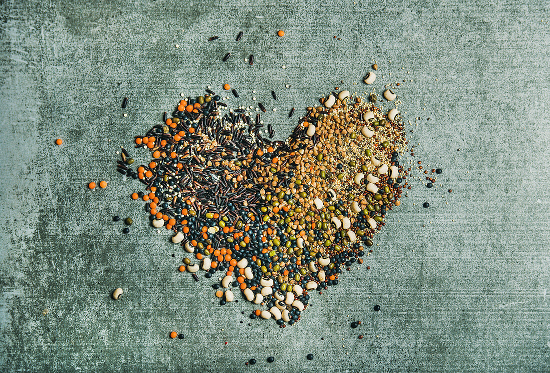 Various raw uncooked grains, beans, cereals in shape of heart