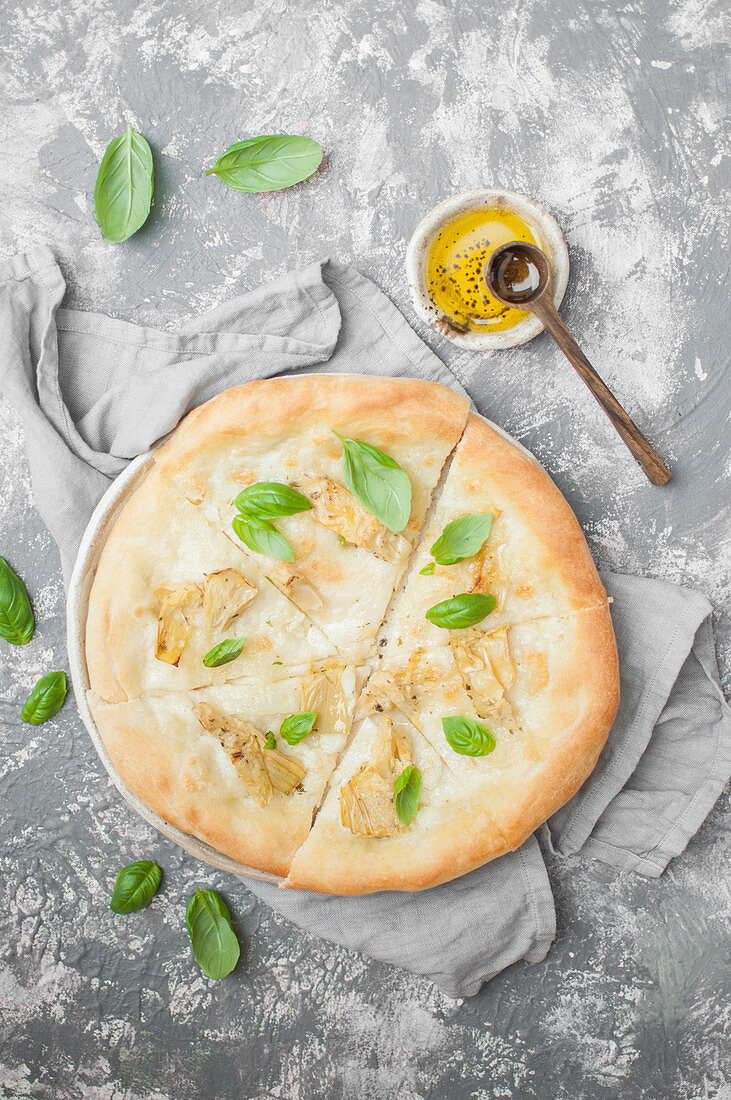 Pizza Bianca mit Artischocken und Mozzarella di Bufala, serviert mit frischem Basilikum und Olivenöl