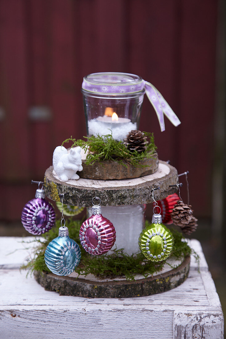 Festive arrangement of slices of tree trunk decorated with candle lantern and Christmas-tree baubles