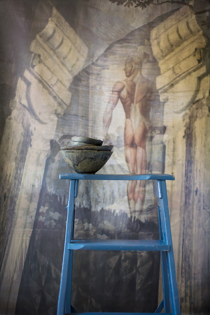 Stack of dark bowls on blue ladder in front of mural