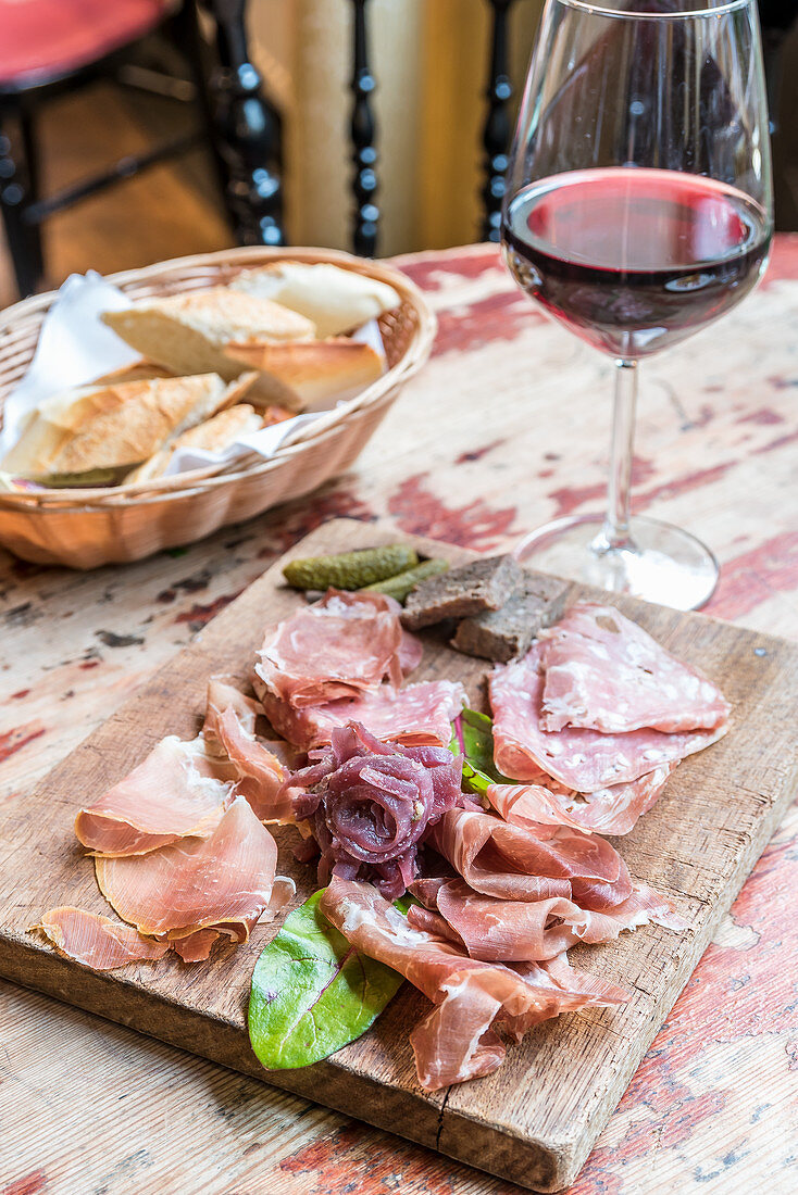 Wurstplatte mit Salami und Schinken, Rotwein und Weißbrot im Hintergrund
