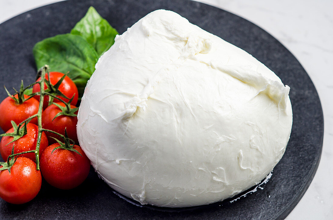 Fresh mozzarella garnished with cherry tomatoes and basil leaves on a dark stone plate
