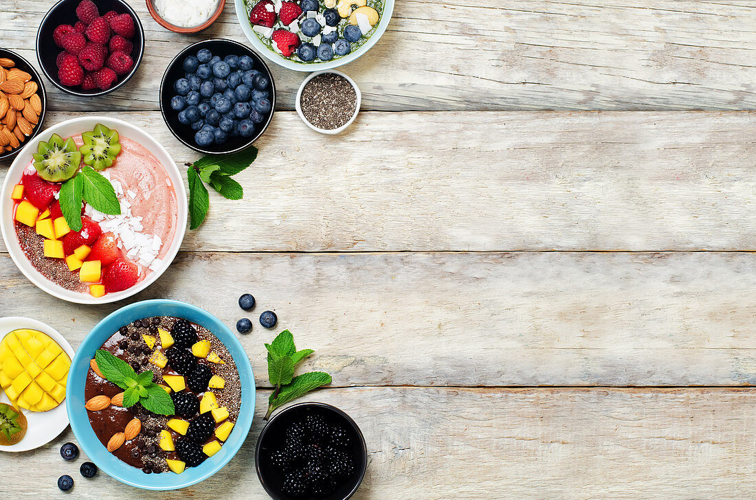 Verschiedene Breakfast bowls und Zutaten auf weißem Holztisch