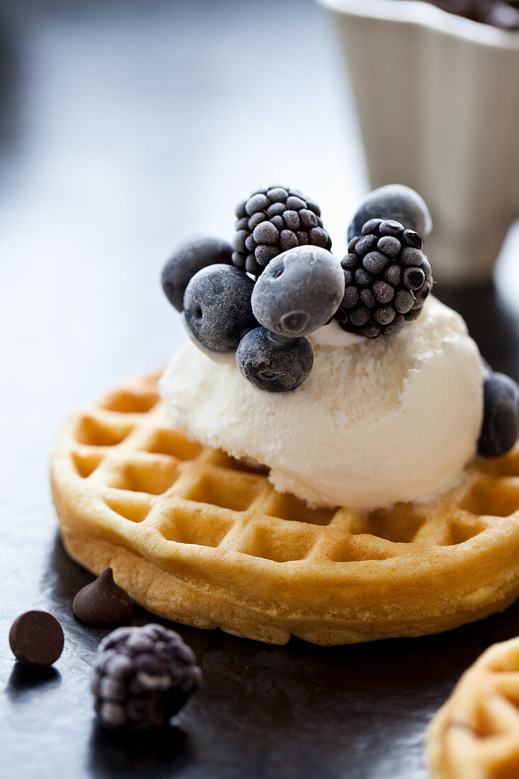 A waffle topped with ice cream and frozen blackberries