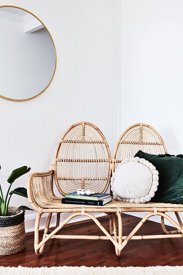 Cushions and books on wicker bench in corner of white room