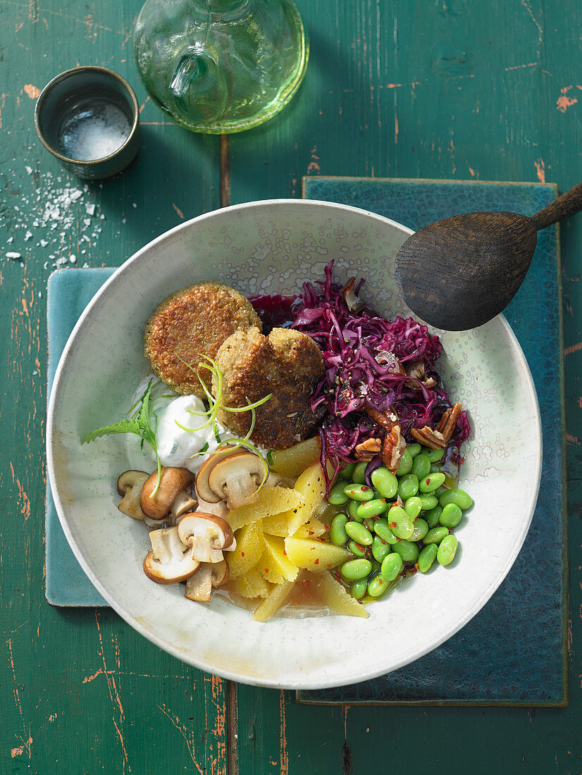 A Buddha Bowl with quinoa fritters, orange and red cabbage salad, mushrooms and edamame beans