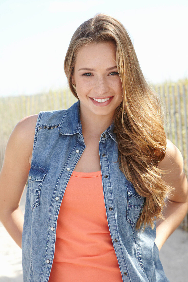 A young blonde woman on a beach wearing an orange top