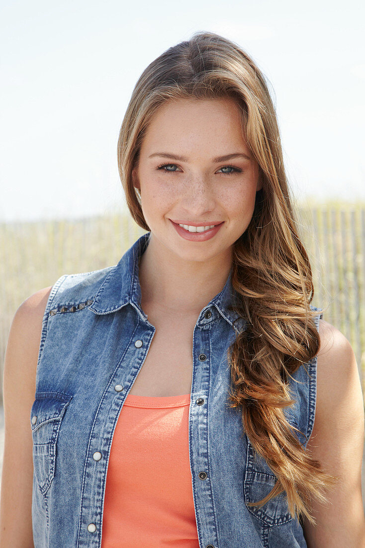 A young blonde woman on a beach wearing an orange top