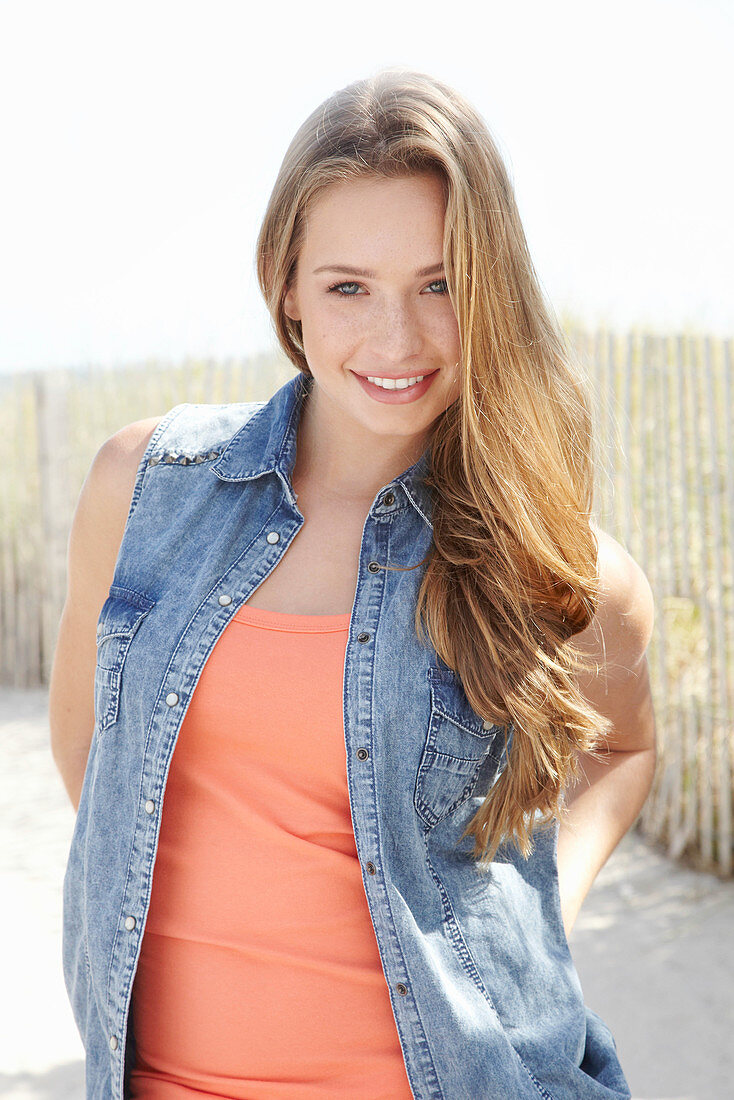 A young blonde woman on a beach wearing an orange top