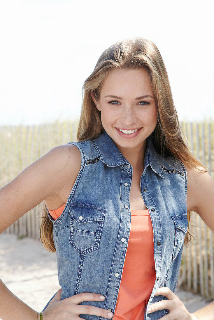 A young blonde woman on a beach wearing an orange top