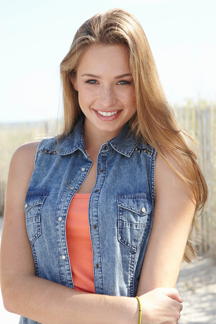 A young blonde woman on a beach wearing an orange top