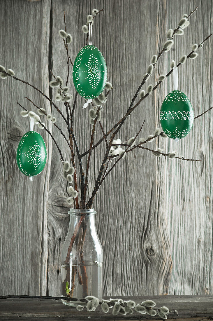 Green-painted Easter eggs hung from pussy willow branches in bottle