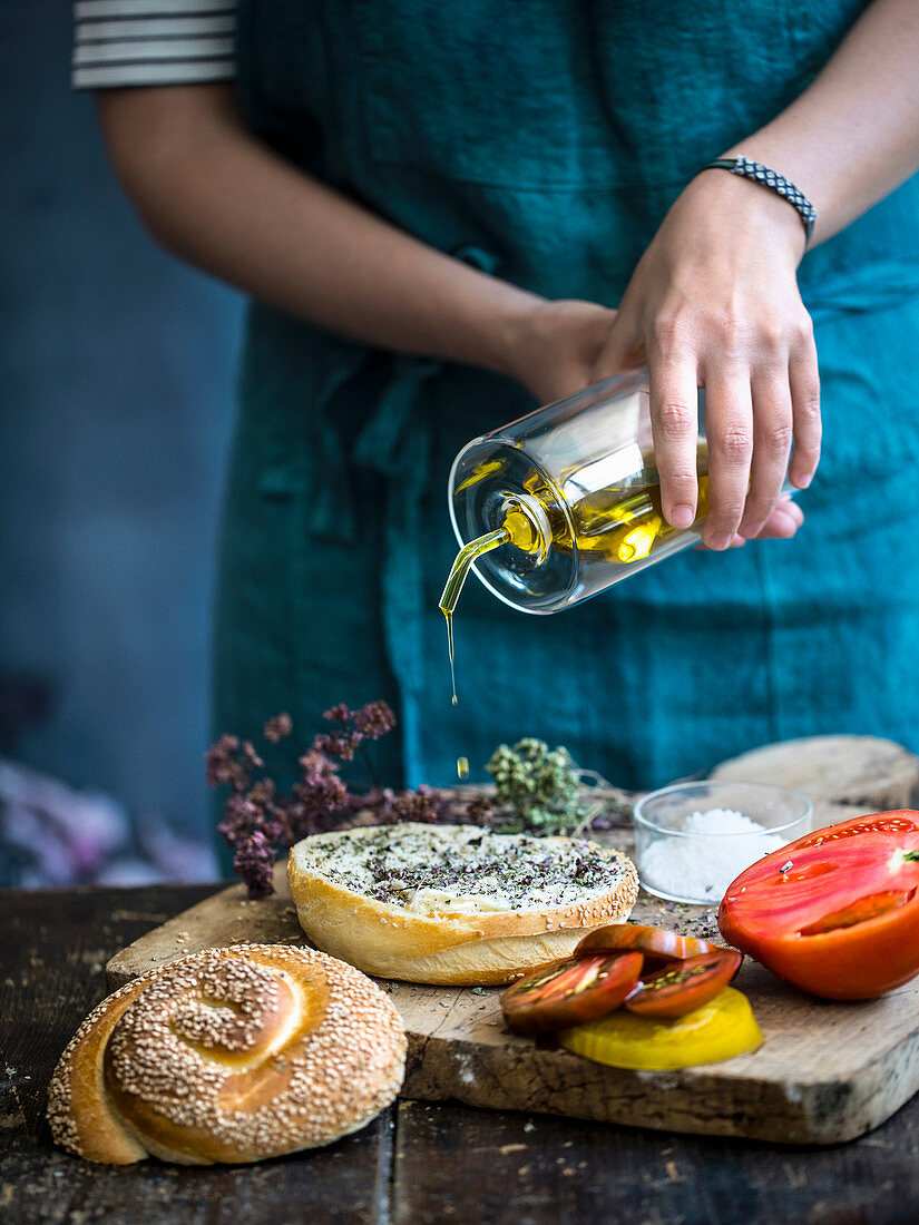 Ein Sesambrötchen vor dem Belegen mit Olivenöl beträufeln