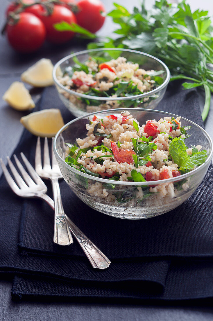 Tabouleh mit Minze, Petersilie, Tomaten und Zitrone in Glasschalen