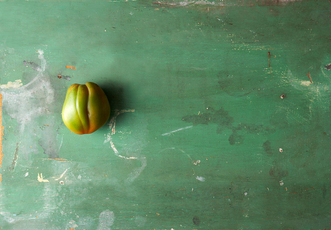 Eine Tomate auf grünem Holzuntergrund