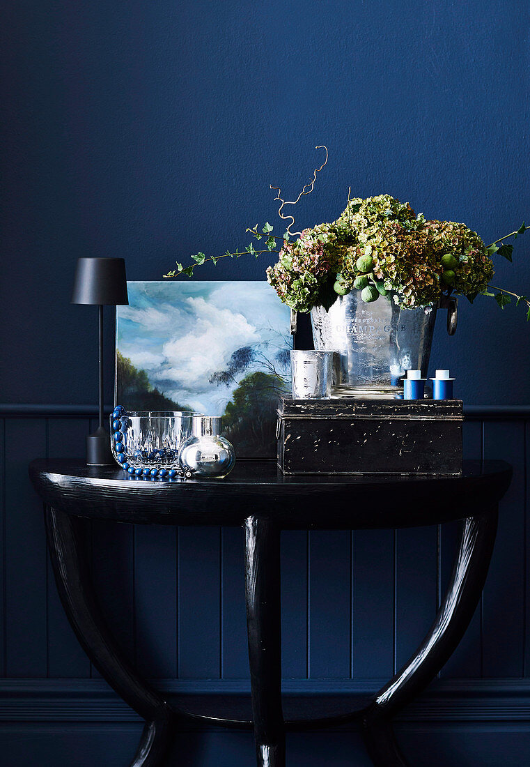 Table lamp, painting, vintage metal box and champagne bucket with flowers on console table