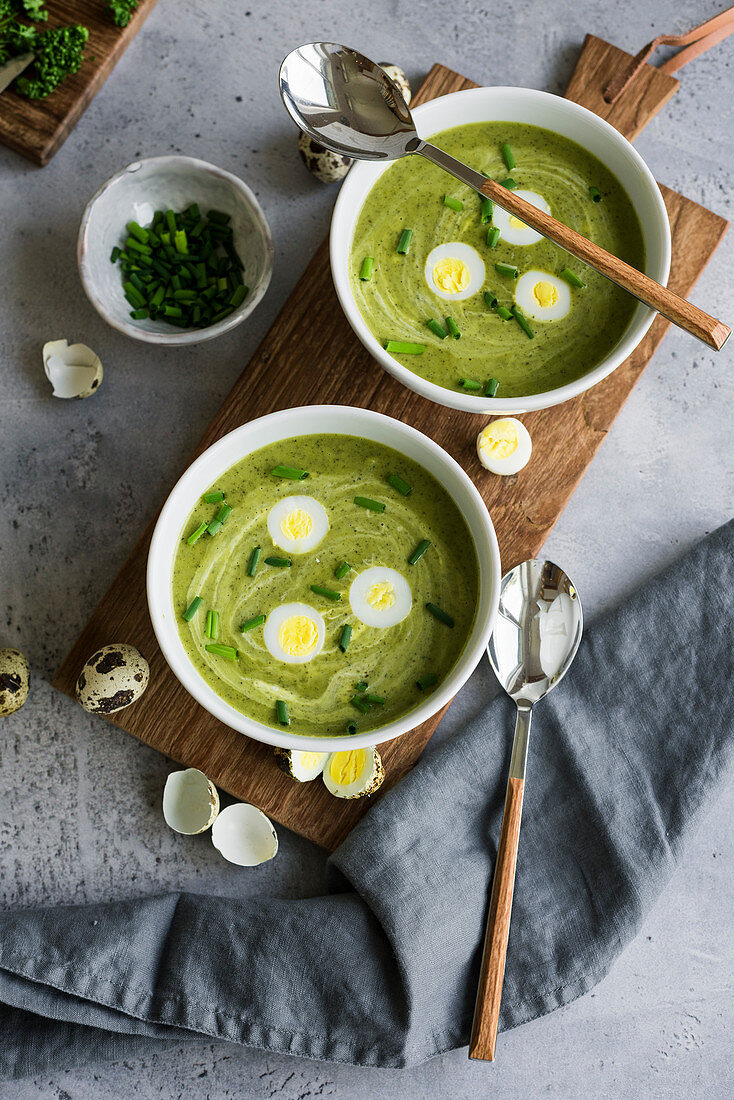 Traditional Frankfurt green herb soup with quail eggs and chives in bowls on a wooden board