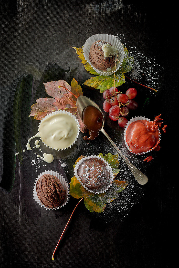 Ice cream desserts and vanilla sauce in paper cases, grapes and autumnal leaves on a black surface
