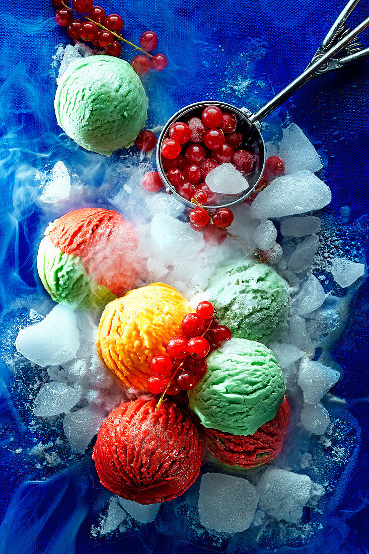 Colourful scoops of ice cream with ice cubes and redcurrants on a blue surface