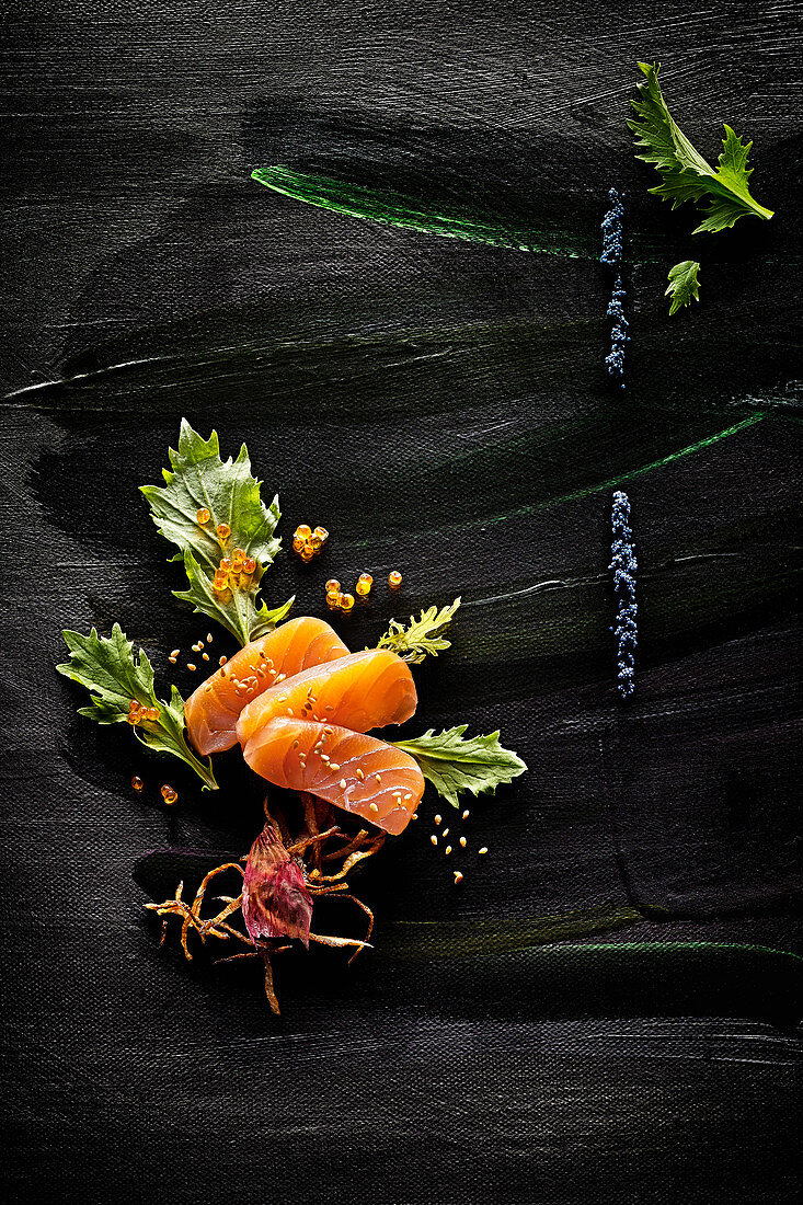 Food-Art: Lachs mit Kaviar, Sellerie, gerösteten Zwiebeln und Sesam auf schwarz bemaltem Untergrund